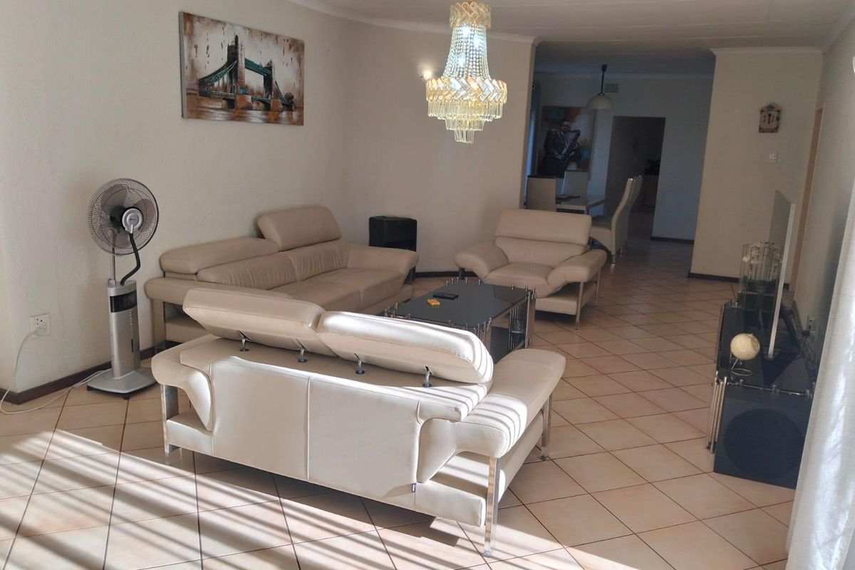 Spacious living room featuring ceramic floor tiles, a decorative crystal chandelier, and coved ceiling details, offering a comfortable and well-lit living space.
