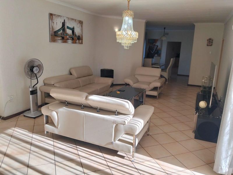 Spacious living room featuring ceramic floor tiles, a decorative crystal chandelier, and coved ceiling details, offering a comfortable and well-lit living space.