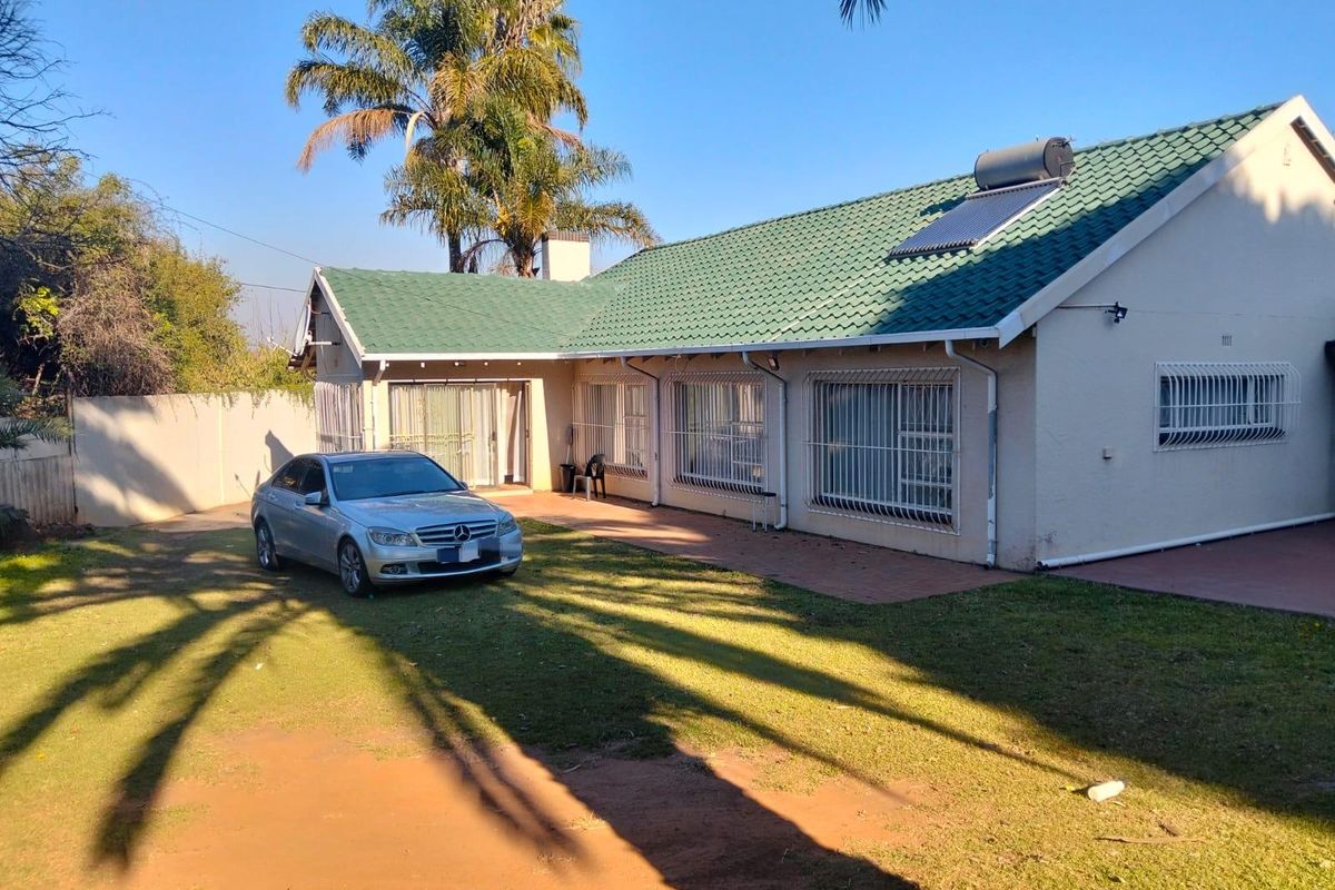 Rear view of the house featuring a tiled roof with solar water heating, security bars on windows, and a paved patio area.