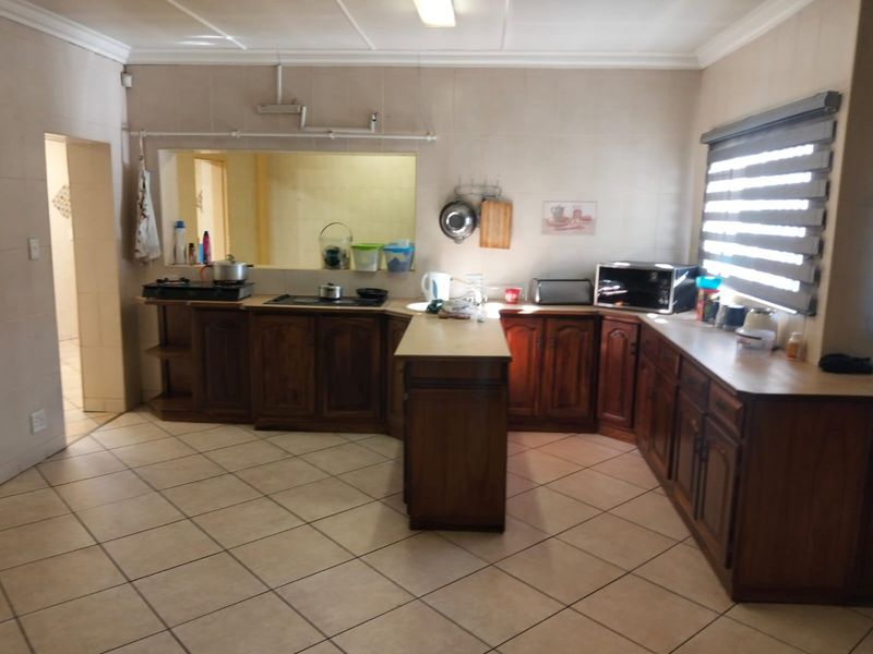 A functional kitchen featuring wooden cabinetry, laminate countertops, and ceramic floor tiles, with a convenient pass-through window to the adjacent living area.