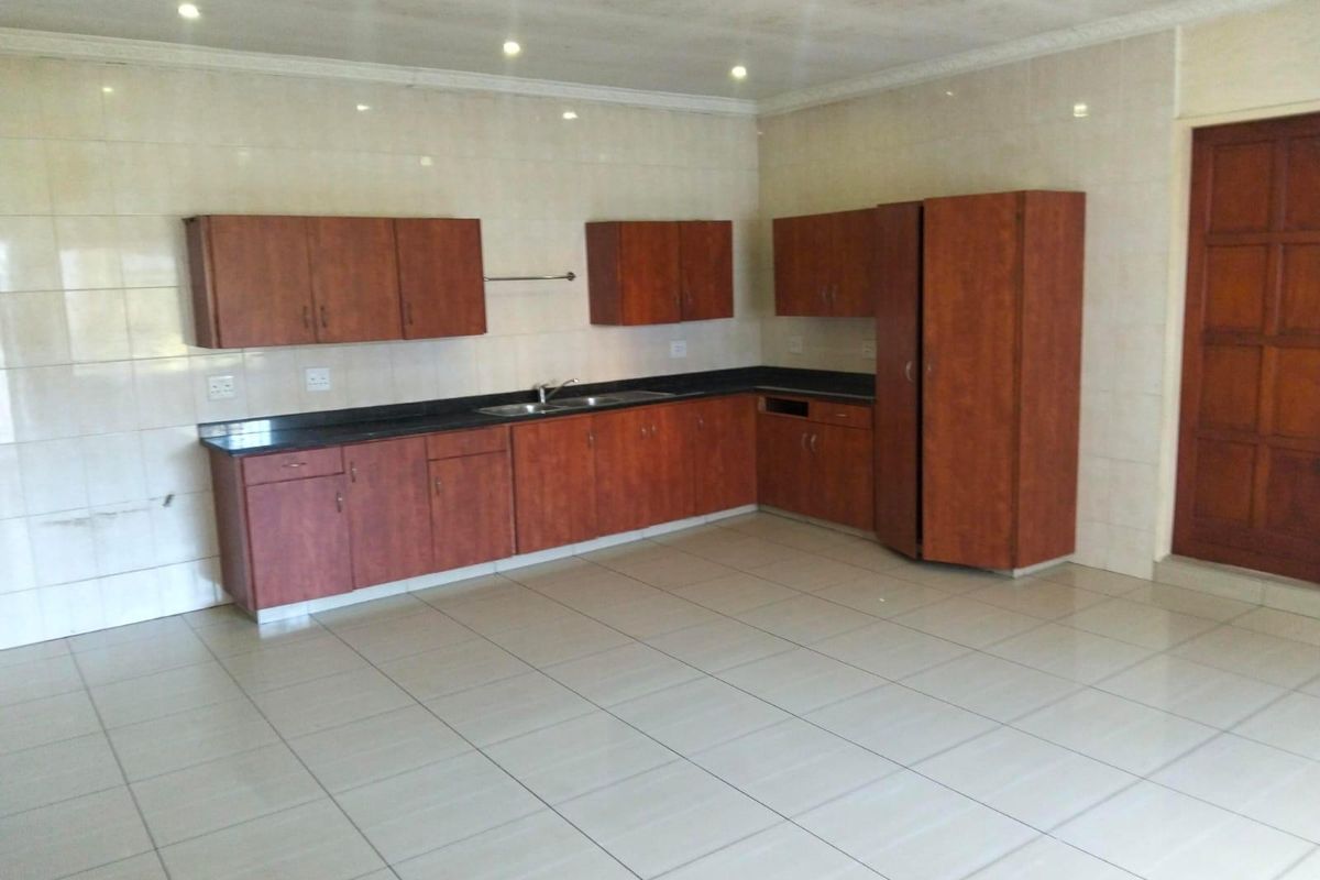 A spacious, empty kitchen featuring wooden cabinetry, dark countertops, tiled walls and flooring, and recessed lighting, offering a functional blank canvas for updates.