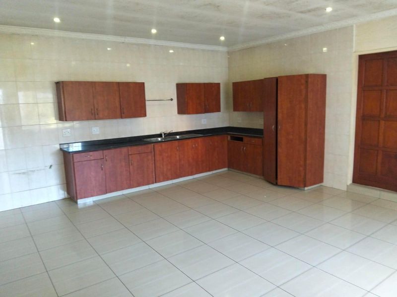 A spacious, empty kitchen featuring wooden cabinetry, dark countertops, tiled walls and flooring, and recessed lighting, offering a functional blank canvas for updates.