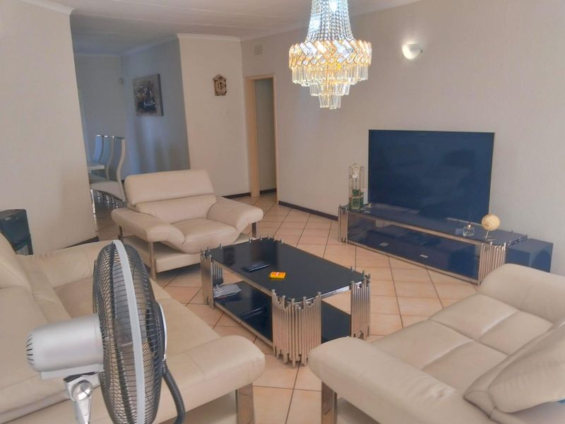 Spacious living room featuring ceramic floor tiles, a decorative crystal chandelier, and coved ceiling detailing, offering a comfortable and well-lit lounge area.