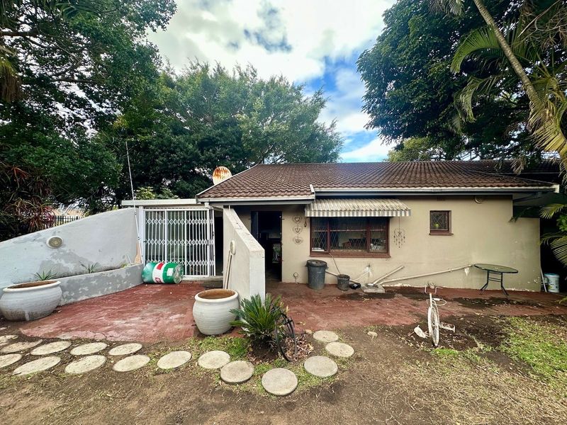 Rear exterior view of the house featuring a tiled roof, concrete patio area, and security gate access.