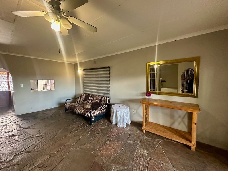 Living room featuring natural stone flooring, a ceiling fan, and a pass-through window connecting to an adjacent space.