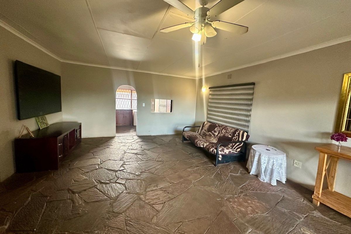 Spacious living room featuring rustic stone flooring, a ceiling fan, and an arched doorway leading to the kitchen area.