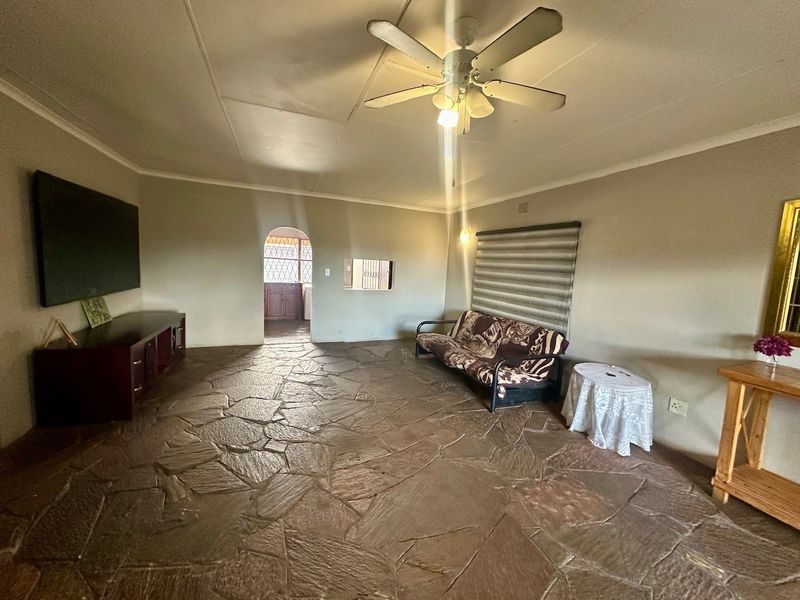 Spacious living room featuring rustic stone flooring, a ceiling fan, and an arched doorway leading to the kitchen area.