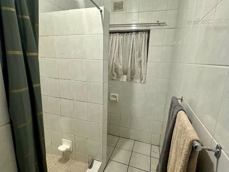 A functional bathroom featuring tiled walls and flooring with a built-in shower partition, requiring cosmetic updates to modernize the space.