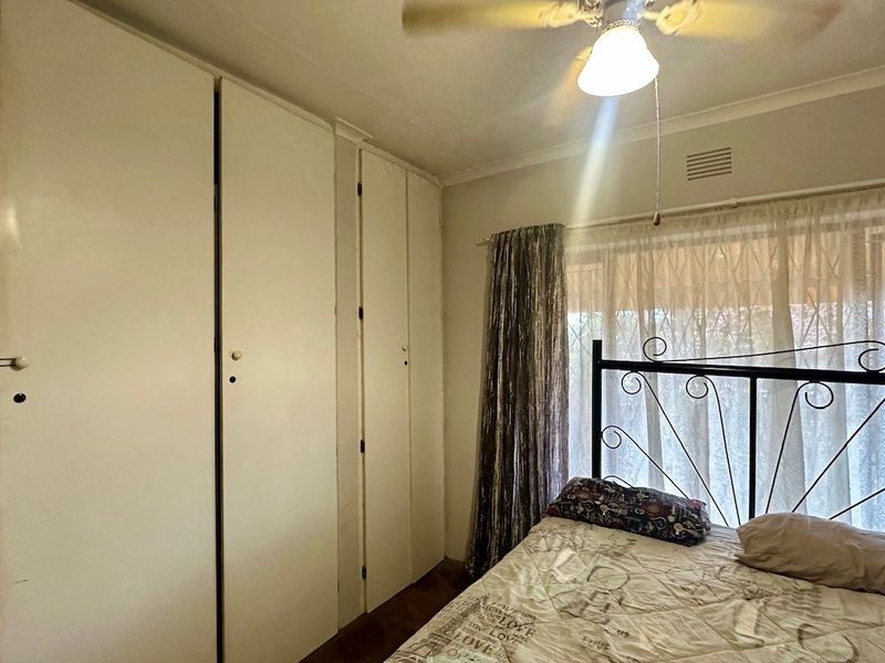 A bedroom featuring built-in cupboards and a ceiling fan, offering a functional space with potential for modern updates.