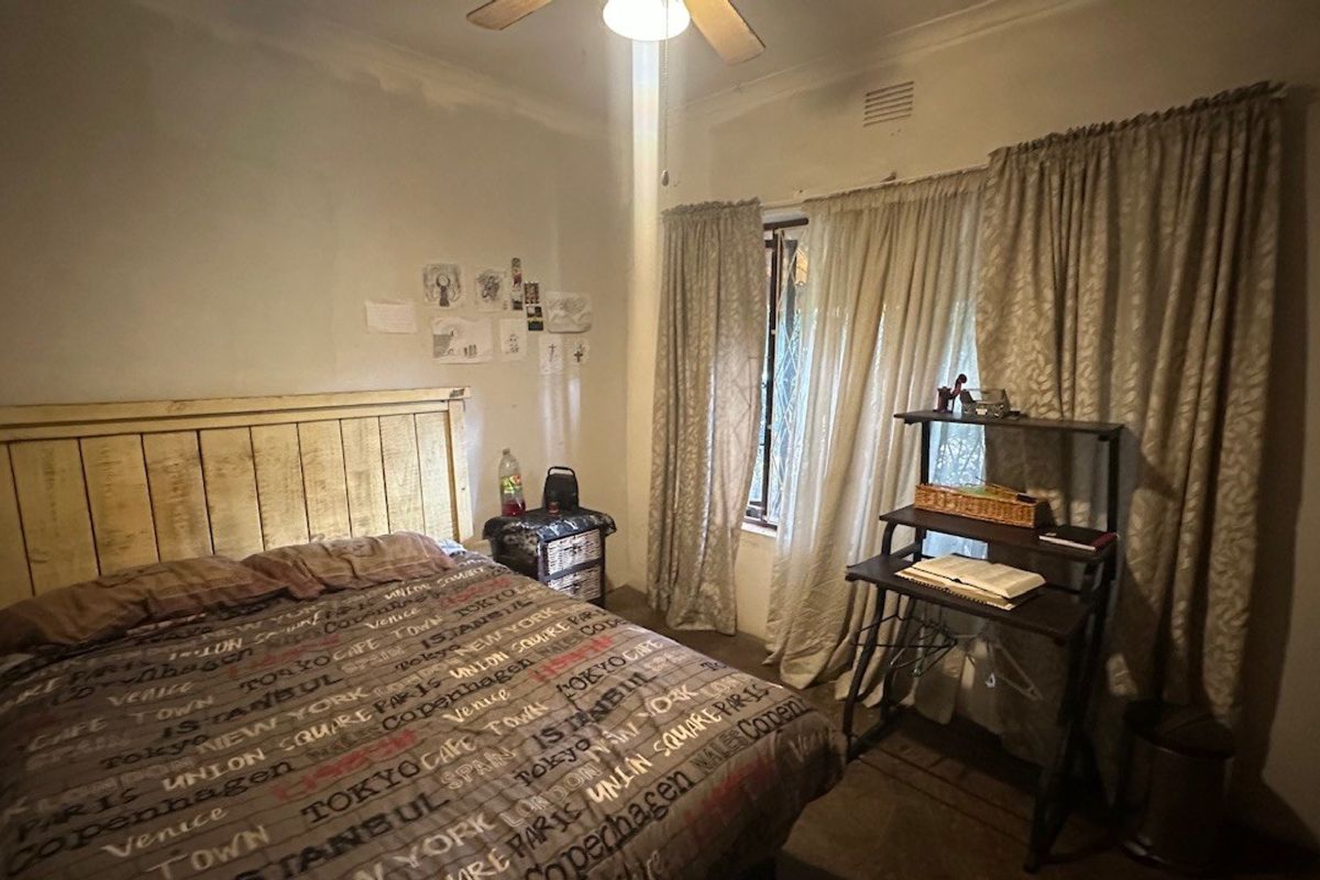 A standard bedroom featuring a ceiling fan, security gate on the window, and curtain rails.