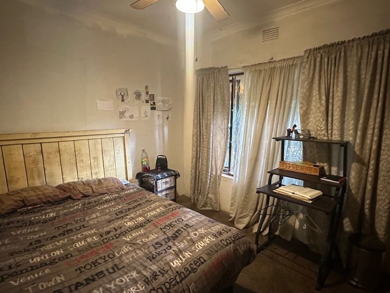 A standard bedroom featuring a ceiling fan, security gate on the window, and curtain rails.