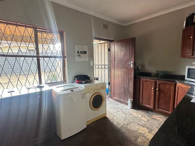 A functional laundry room featuring built-in wooden cabinetry, granite countertops, stone flooring, and direct access to the exterior.
