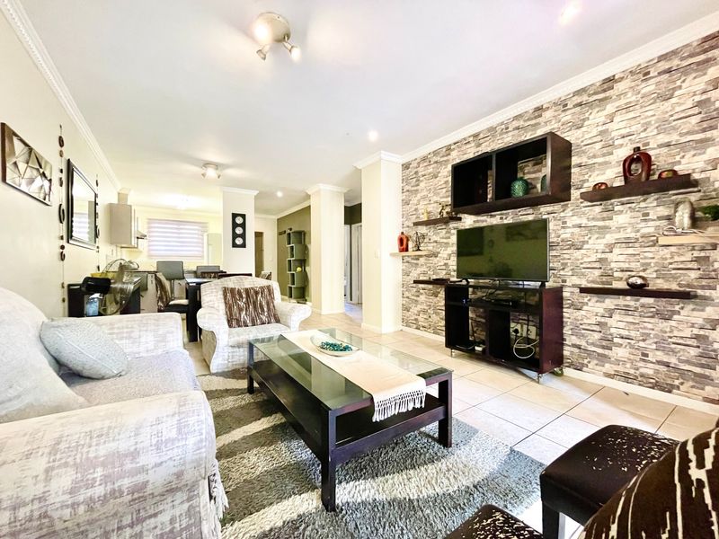 Open-plan living area featuring a stone veneer accent wall, tiled flooring, and recessed lighting, seamlessly connecting to the kitchen space.