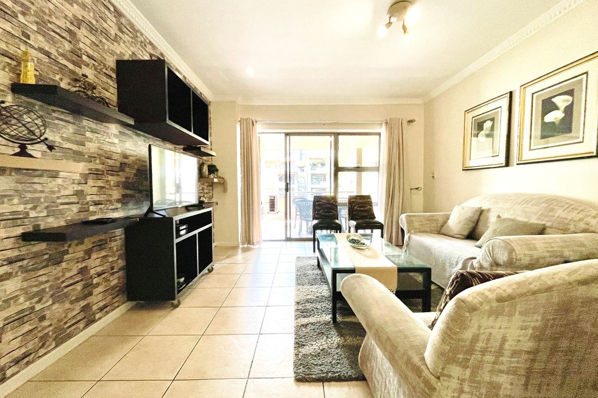A well-maintained living room featuring a stone veneer accent wall, ceramic tiled flooring, and large sliding glass doors leading to an outdoor patio area.