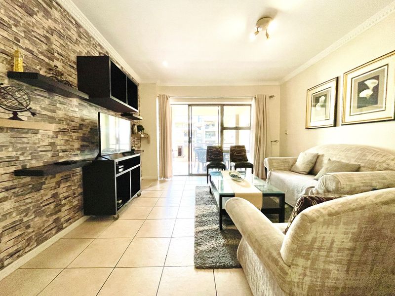 A well-maintained living room featuring a stone veneer accent wall, ceramic tiled flooring, and large sliding glass doors leading to an outdoor patio area.