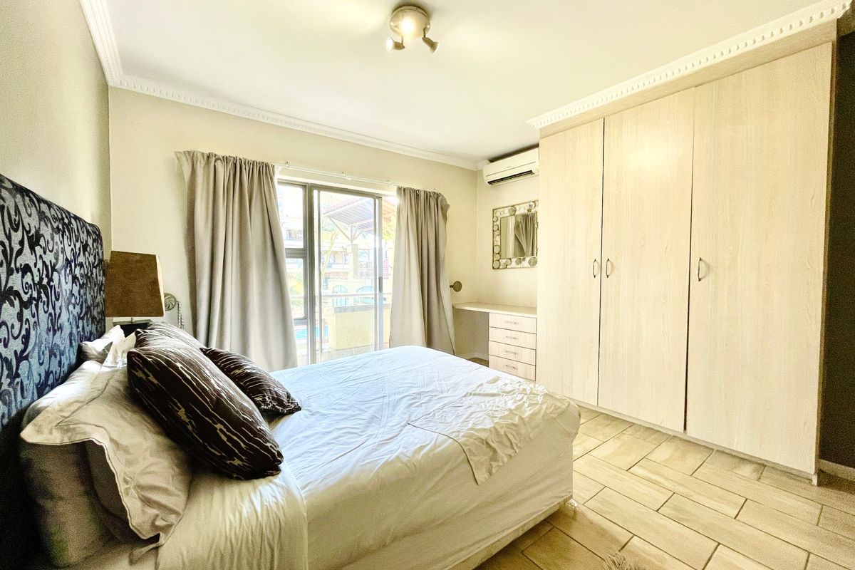 A well-lit bedroom featuring built-in wooden cupboards, tiled flooring, an air conditioning unit, and a sliding glass door providing access to the exterior.