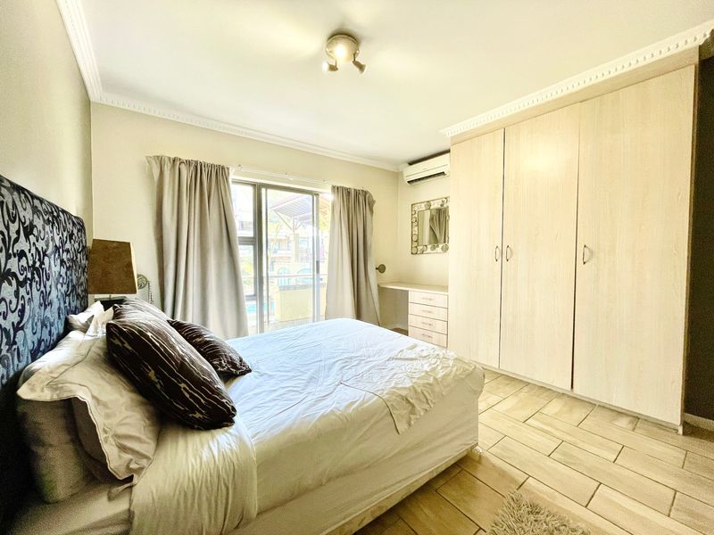A well-lit bedroom featuring built-in wooden cupboards, tiled flooring, an air conditioning unit, and a sliding glass door providing access to the exterior.