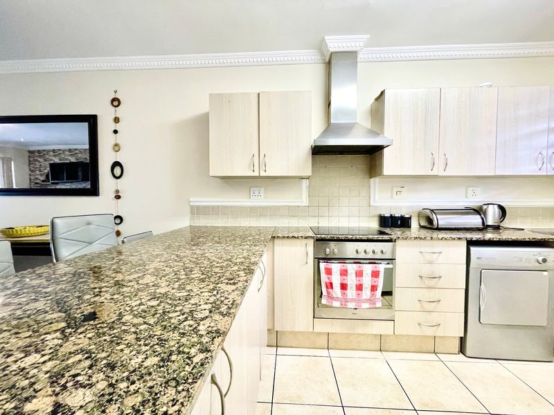A functional kitchen featuring granite countertops, light wood cabinetry, a built-in oven with hob, stainless steel extractor fan, and tiled flooring.