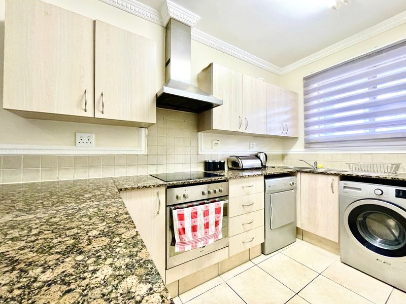 Functional kitchen featuring granite countertops, built-in cabinetry, stainless steel oven and hob, tiled backsplash, and integrated laundry appliance space.