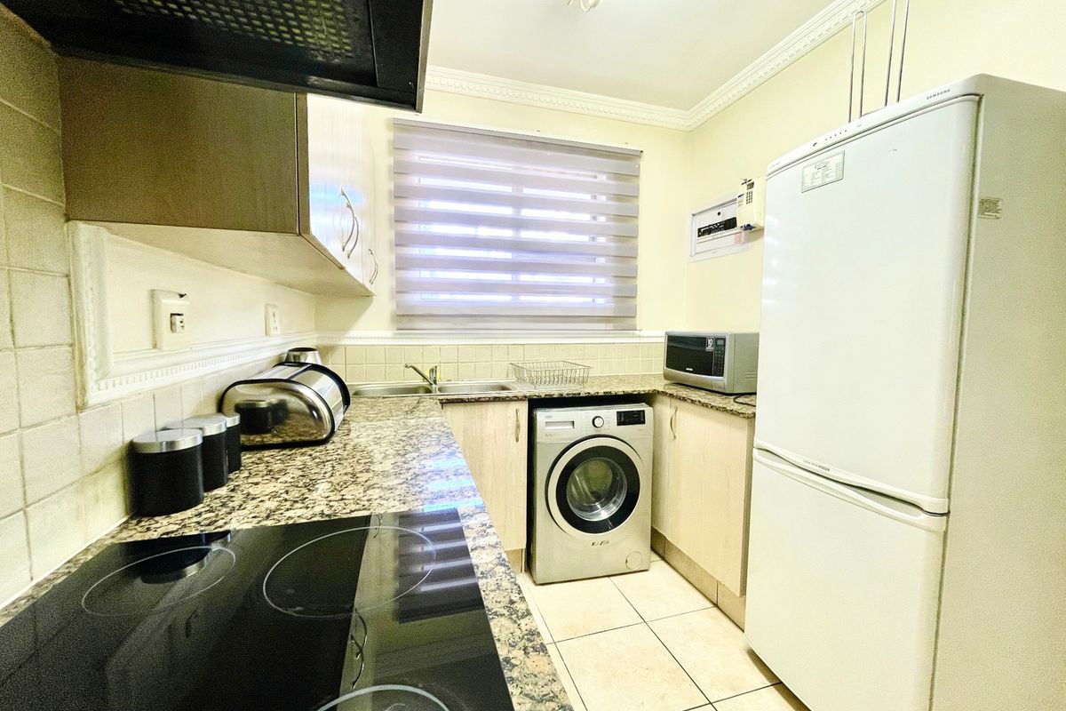A functional kitchen featuring granite countertops, built-in cabinetry, an electric hob with extractor fan, and tiled flooring.
