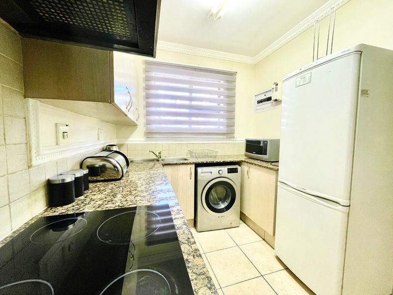 A functional kitchen featuring granite countertops, built-in cabinetry, an electric hob with extractor fan, and tiled flooring.