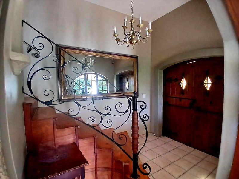 Welcoming entrance hall featuring a classic wooden staircase with ornate wrought iron balustrades, double timber front doors, and tiled flooring.