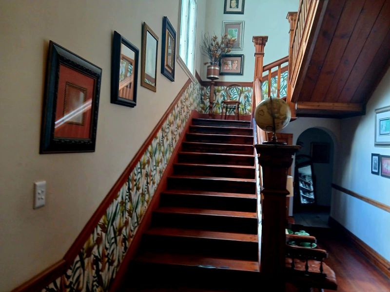 A traditional hallway featuring a wooden staircase with a decorative handrail and patterned wallpaper accents.