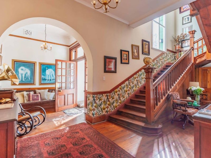 Grand entrance hall featuring a classic timber staircase, polished wooden floors, and a charming arched entryway with built-in seating.