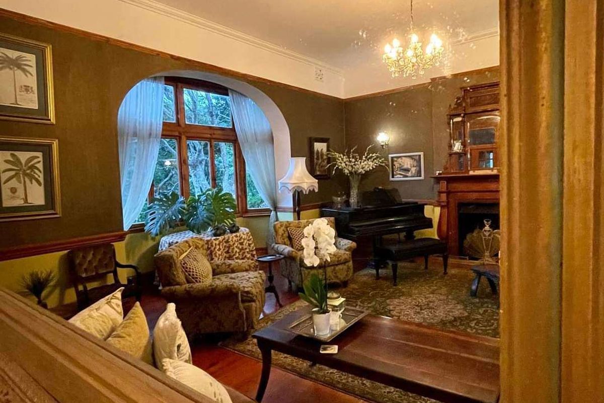 Spacious living room featuring a traditional fireplace with timber mantelpiece, arched window, ceiling rose, and classic timber flooring.