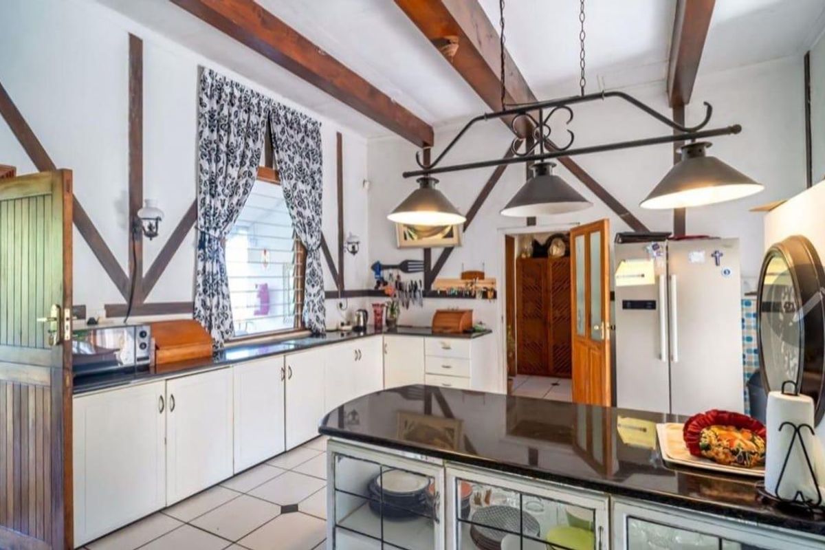 A rustic-style kitchen featuring exposed timber ceiling beams, granite countertops, a central island, and tiled flooring with decorative wall trim.