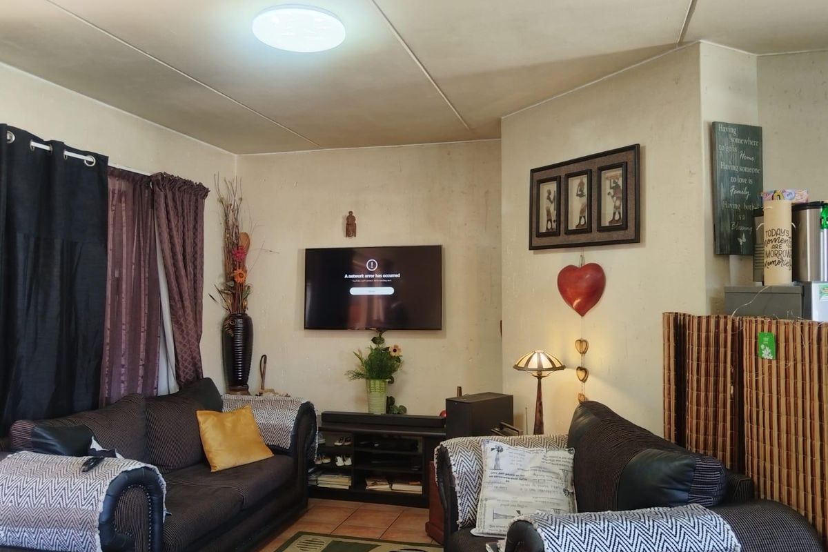 A living room area featuring tiled flooring and standard ceiling lighting, currently showing signs of wear on the wall surfaces.