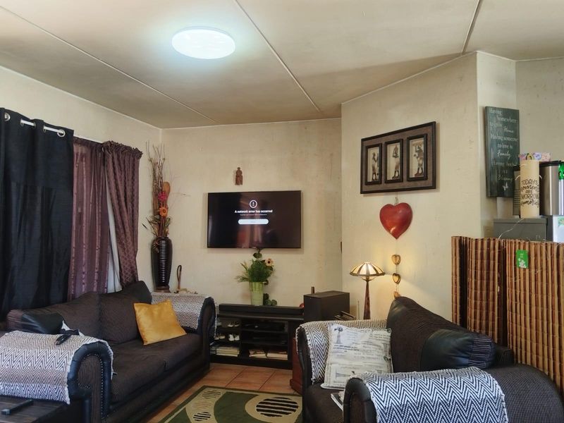 A living room area featuring tiled flooring and standard ceiling lighting, currently showing signs of wear on the wall surfaces.