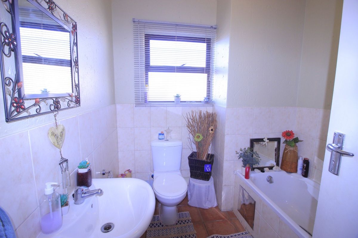 A functional bathroom featuring a pedestal basin, toilet, and bathtub with neutral wall and floor tiling.