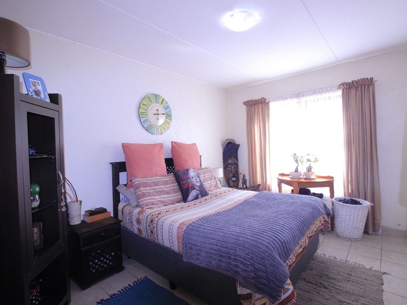 A functional bedroom featuring tiled flooring, neutral wall finishes, and natural light provided by a window with curtain rails.