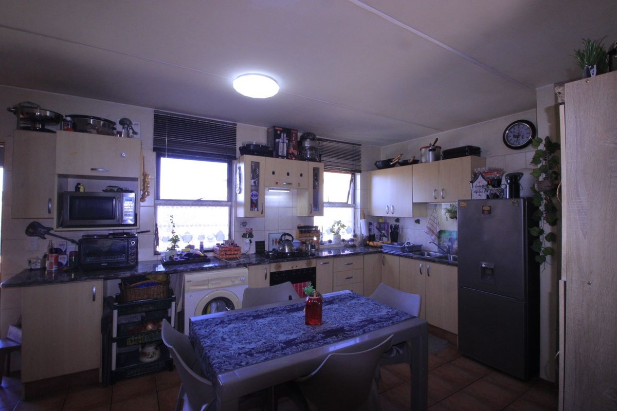 A functional kitchen featuring built-in cabinetry, laminate countertops, a built-in oven, hob, and integrated laundry plumbing, finished with tiled flooring.