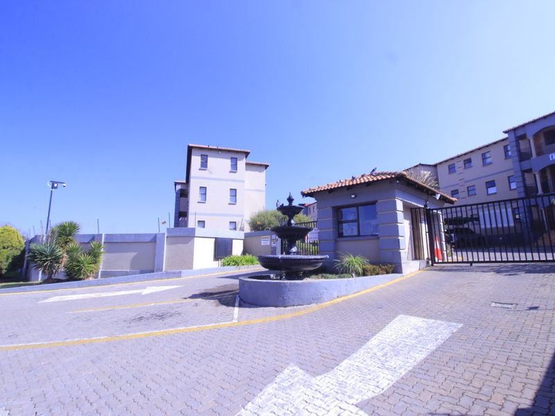 The apartment complex entrance features a secure gated access point, a guard house, and a decorative water fountain in the paved driveway area.