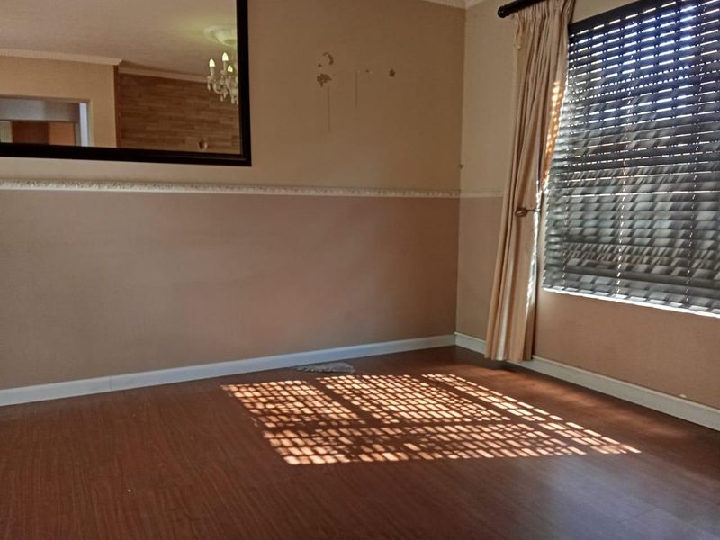 An empty living room featuring laminate flooring, a dado rail, and venetian blinds, showing signs of wear on the wall surfaces.