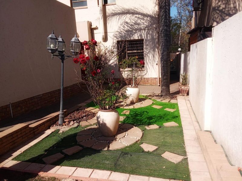 A compact rear courtyard featuring a paved walkway, artificial grass sections, and a decorative lamp post, enclosed by high boundary walls.
