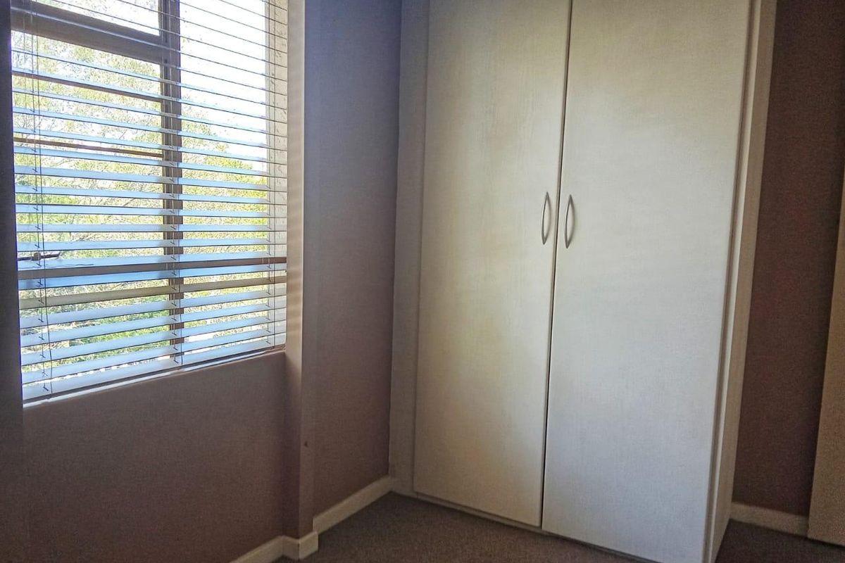 A vacant bedroom featuring neutral wall tones, carpeted flooring, a built-in wardrobe, and a window fitted with venetian blinds.