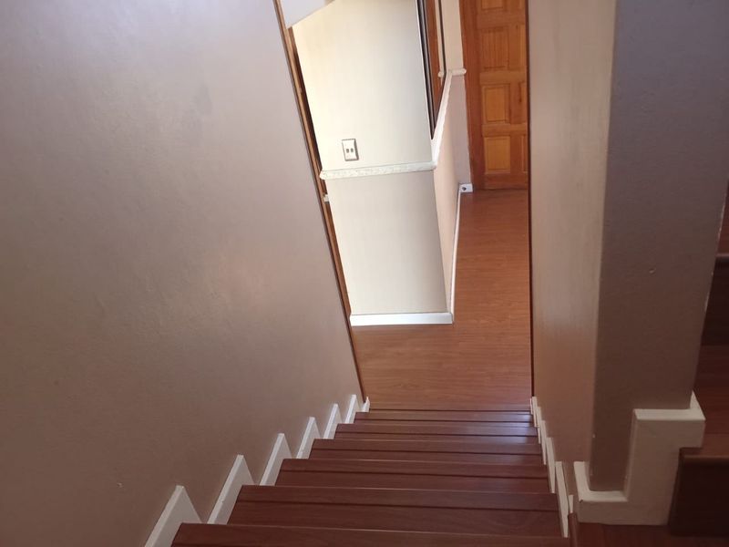 A view looking down a wooden staircase into a hallway with laminate flooring and neutral wall finishes.