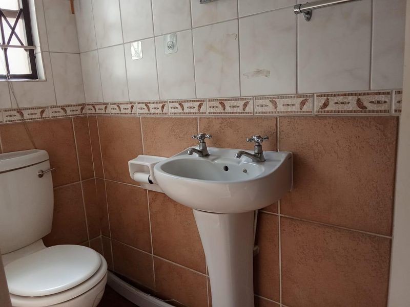 A functional bathroom featuring a pedestal basin, ceramic toilet, and tiled walls with decorative border accents.