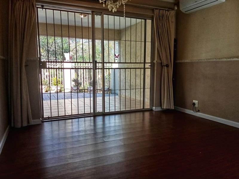 A vacant living room featuring dark laminate flooring, a split-system air conditioner, and a sliding glass door leading to an outdoor patio area.