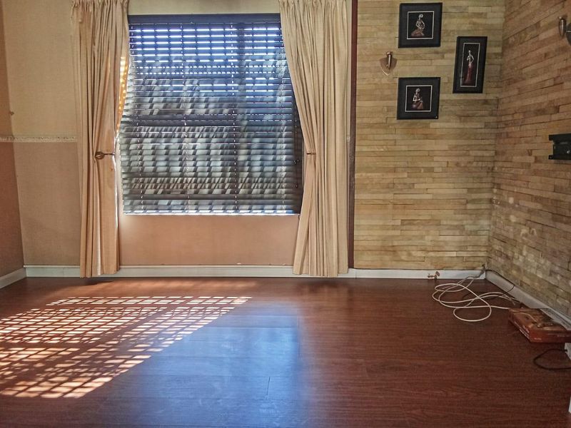 A bright, empty living room featuring laminate flooring and a textured stone cladding feature wall with natural light filtering through venetian blinds.