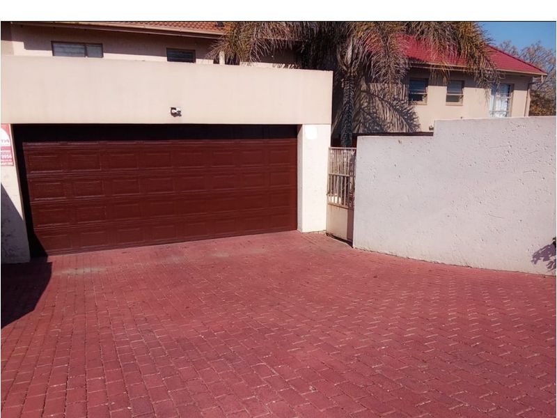Front exterior view of the townhouse featuring a double garage, paved driveway, and secure boundary wall access.