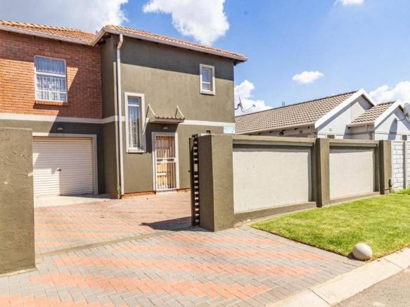 Front exterior view of a two-story house featuring a brick-paved driveway, secure perimeter wall, and integrated garage.