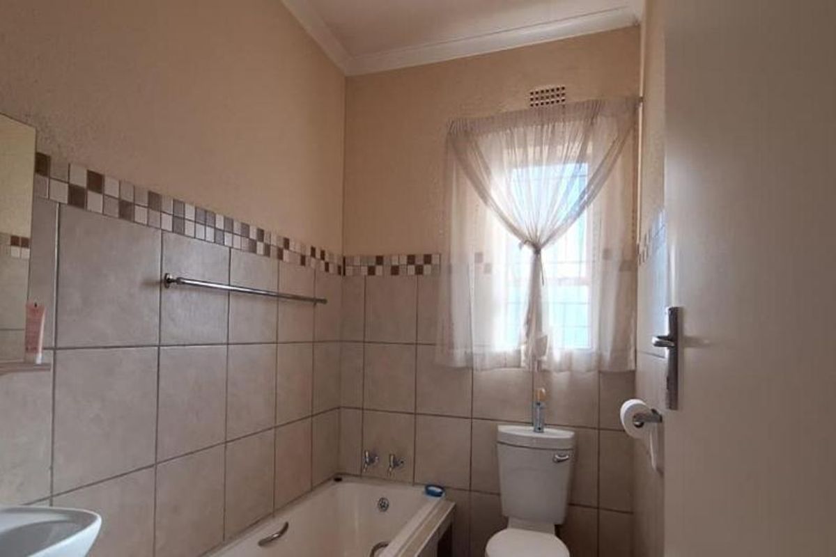 A functional bathroom featuring a bathtub, pedestal basin, and toilet with neutral wall tiling and a window for natural light.