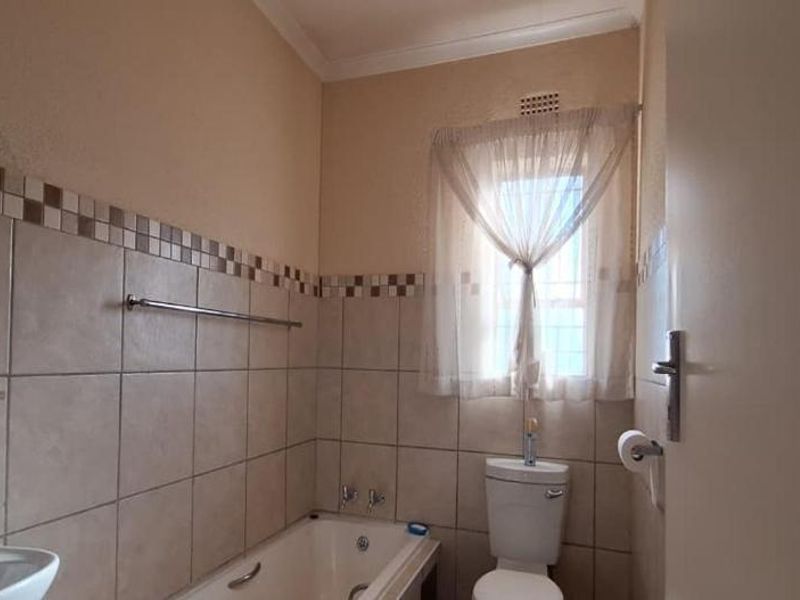 A functional bathroom featuring a bathtub, pedestal basin, and toilet with neutral wall tiling and a window for natural light.