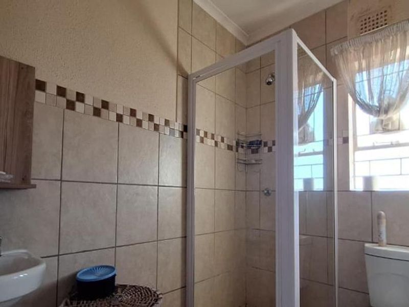 A functional bathroom featuring a shower enclosure, pedestal basin, and toilet, finished with neutral ceramic wall tiles and a window for natural light.