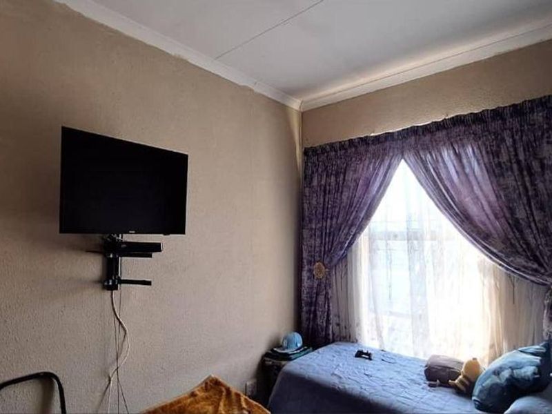 A compact bedroom featuring a window with curtains and wall-mounted television bracket.
