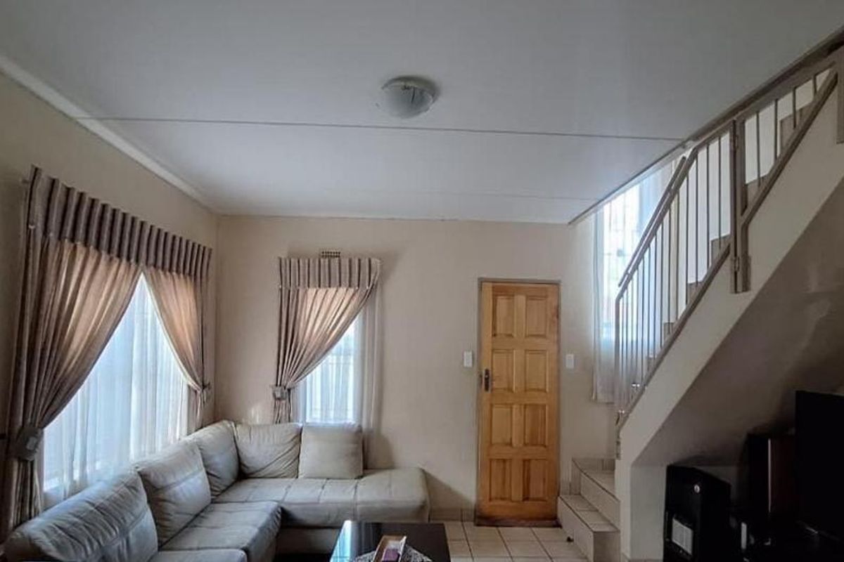 A living room featuring tiled flooring, a wooden entrance door, and an internal staircase with a metal balustrade.